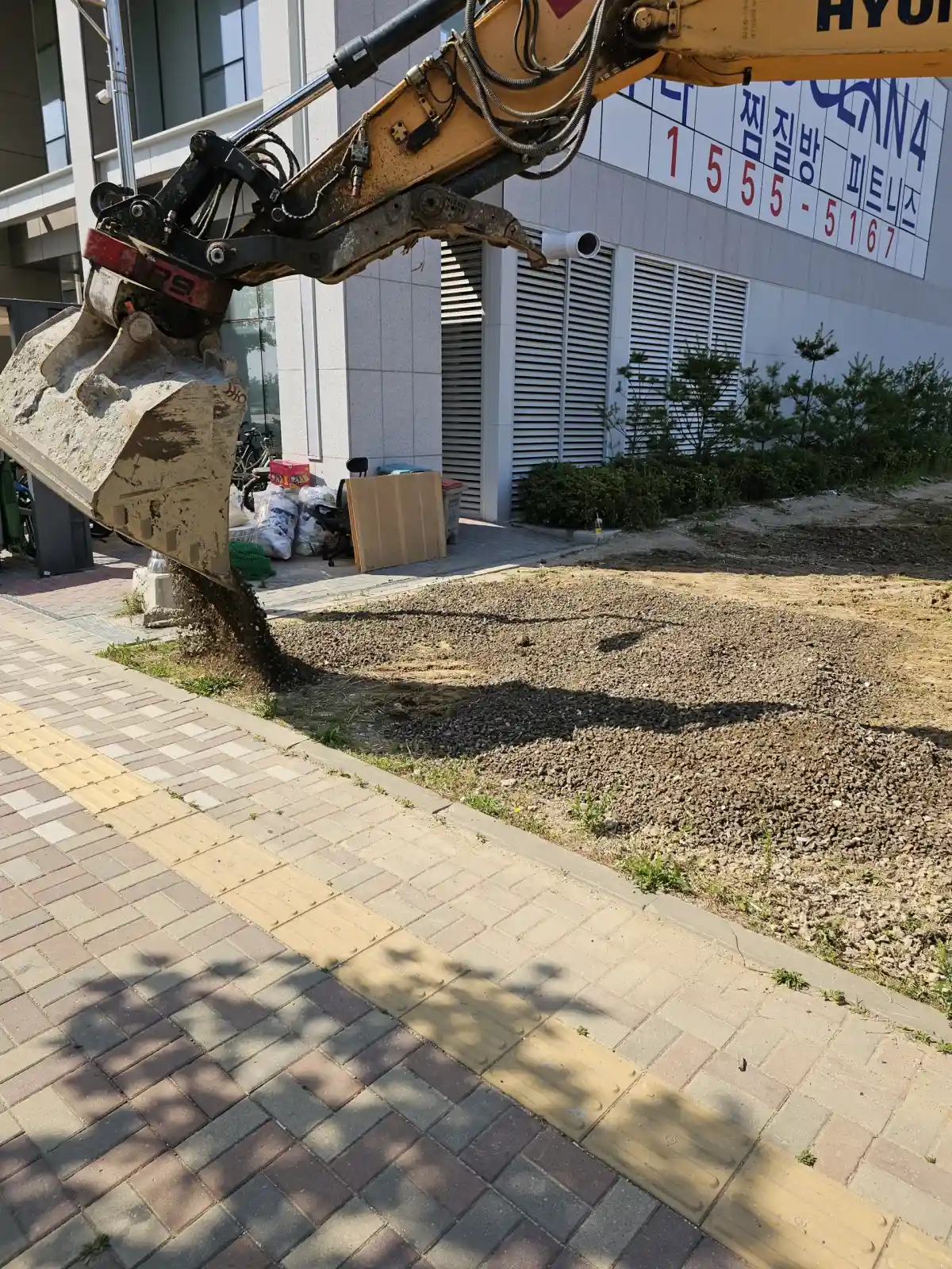 굴착기 버킷으로 흙과 자갈을 긁어 고르는 주차장 바닥 평탄화 작업