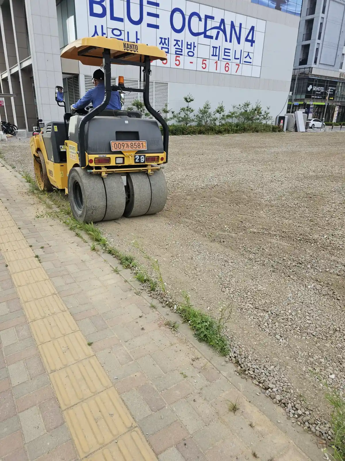 3륜 진동 롤러가 쇄석 노면을 다지는 주차장 노반 다짐 장면